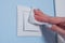 Woman cleaning light switch on blue wall with wet wipe - disinfection concept