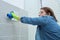 Woman cleaning and polishing chrome toilet button on tiled wall