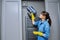 Woman cleaning wall-mounted hood ventilation grill in bathroom with vacuum cleaner