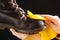 A woman cleans brown nubuck boots on a black background, wipes the dust with a yellow shoe rag.