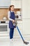 A woman cleans the floor with a cleaning vacuum cleaner in a modern kitchen.