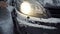 A woman clears snow from her car\'s headlights on a frosty day