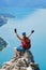 Woman with climbing helmet and via ferrata gear sits on top of a rock at Attersee, Austria, and spreads her arms. Happiness.