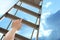 Woman climbing up stepladder against sky with clouds, closeup