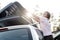 Woman closes a trunk loaded with things, which is on the roof of a car, summer day. Family vacation.