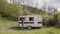 Woman comes to abandoned retro caravan in wild area and sits down on mountain background