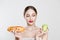 Woman compare tasty unhealthy burger sandwich hotdog in hand and green apple getting ready to eat healthy food isolated on a white