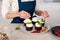 Woman confectioner in blue apron decorating creamy top of tasty cupcake with fresh berries and mint at kitchen