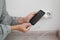 Woman connecting charger cable to mobile phone near white brick wall indoors, closeup