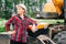 Woman in construction clothes with a white helmet in a plaid shirt on the background of an excavator