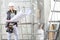 Woman construction worker builder looking at bluprint, wearing helmet, hearing protection headphones and tools belt bag in