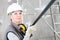Woman construction worker builder portrait wearing white helmet and hearing protection headphones, holding a metal stud for