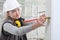 Woman construction worker work with meter tape and pencil, measure wall in interior building site, wearing helmet, glasses and