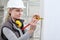 Woman construction worker work with meter tape and pencil, measure wall in interior building site, wearing helmet and hearing