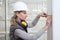 Woman construction worker work with meter tape and pencil, measure wall in interior building site, wearing helmet and hearing