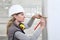 Woman construction worker work with meter tape and pencil, measure wall in interior building site, wearing helmet and hearing