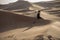 A woman contemplates in sand dunes during sunset.