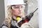 Woman contruction worker using cordless drill driver making a hole in wall, builder with safety hard hat, hearing protection