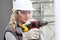 Woman contruction worker using cordless drill driver making a hole in wall, builder with safety hard hat, hearing protection