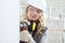 Woman contruction worker using cordless drill driver making a hole in wall, builder with safety hard hat, hearing protection