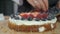 Woman cooking berry cake and decorating biscuit with raspberries