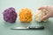 Woman cooking colorful rainbow cauliflower in purple, orange and white in row with knife on pastel green background