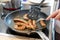 Woman cooking sausages in pan on kitchen cooking plate with fork and black spatula with delicious fatty bratwurst for dinner as un