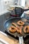 Woman cooking sausages in pan on kitchen cooking plate with fork and black spatula with delicious fatty bratwurst for dinner as un