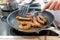 Woman cooking sausages in pan on kitchen cooking plate with fork and black spatula with delicious fatty bratwurst for dinner as un