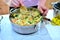 Woman cooks boiled rice with vegetables in a saucepan. Green beans, peppers, corn, peas, onions and carrots are prepared without