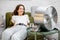 Woman cooling herself with a fan at home