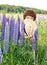 A woman covers her mouth and nose with a straw hat from the pollen of flowering lupins