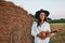 Woman in cowboy hat staying with guitar near a straw bale. Summer, beauty, fashion, glamour, lifestyle concept. Cottagecore