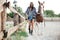 Woman cowgirl in hat walking with her horse in village