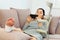 Woman with crutches lying on couch and using smartphone