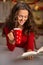 Woman with cup of chocolate and book in Christmas kitchen