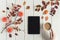 Woman with cup of coffee and tablet, leaves, rowan and small pumpkins on white retro wood boards. background. Autumn, fall concept