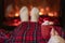 Woman with cup of hot cocoa and marshmallow warming legs in winter white socks near fireplace flame, covered christmas plaid.