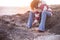 Woman with curly hair and flared trousers and rock rodipinge sweater at sunset sitting on a rock at an isolated beach