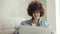 Woman with curly hair writing message in social media on laptop sitting on sofa.
