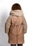 Woman with curly red hair in mini beige sheepskin coat combined with textile sleeves and knitted scarf stands back to us