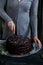 Woman cuts chocolate cake close. Dark tones