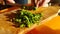 Woman cuts green onion knife on wooden board in kitchen in sunlight