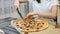 Woman cuts a hot pizza with mushrooms, cheese, maize, olives, red onion rings and tomatoes in a cardboard box using