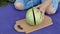 Woman cuts a watermelon in half on a wooden board while sitting on a blue rug in the garden. Close-up