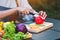 A woman cutting and chopping red bell pepers by knife on wooden board with mixed vegetables in a tray