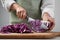 Woman cutting fresh radicchio cabbage on board at wooden table, closeup