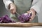 Woman cutting fresh radicchio cabbage on board at wooden table, closeup