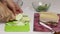 The woman is cutting the onion. The chopped fat lies on the board. Container contains parsley and garlic. Salted lard with herbs