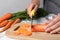 Woman cutting ripe carrot on board at table, closeup